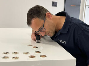Techniker prüft eine colorierte Münze mit einem Fadenzähler auf Qualität